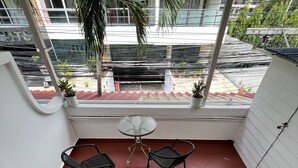 Een balkon met twee stoelen en een kleine tafel, een trap met waarschuwingstape, en uitzicht op gebouwen en groen.