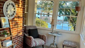 A cozy room with a brick wall, a patterned armchair, a small table, a colorful rug, and a window with a view of the outside. - Charming home in downtown Camden (Camden)