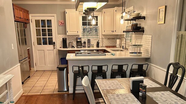 A kitchen with white cabinets, a central island with bar stools, a refrigerator, and a dining table with placemats. - Charming home in downtown Camden (Camden)