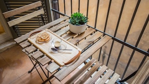 Una mesa de madera con una bandeja que sostiene una taza de café y un plato de comida, una planta en maceta y un banco de madera.