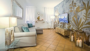 Una sala de estar con un sofá, un televisor, una lámpara y una pared con un diseño de hojas.