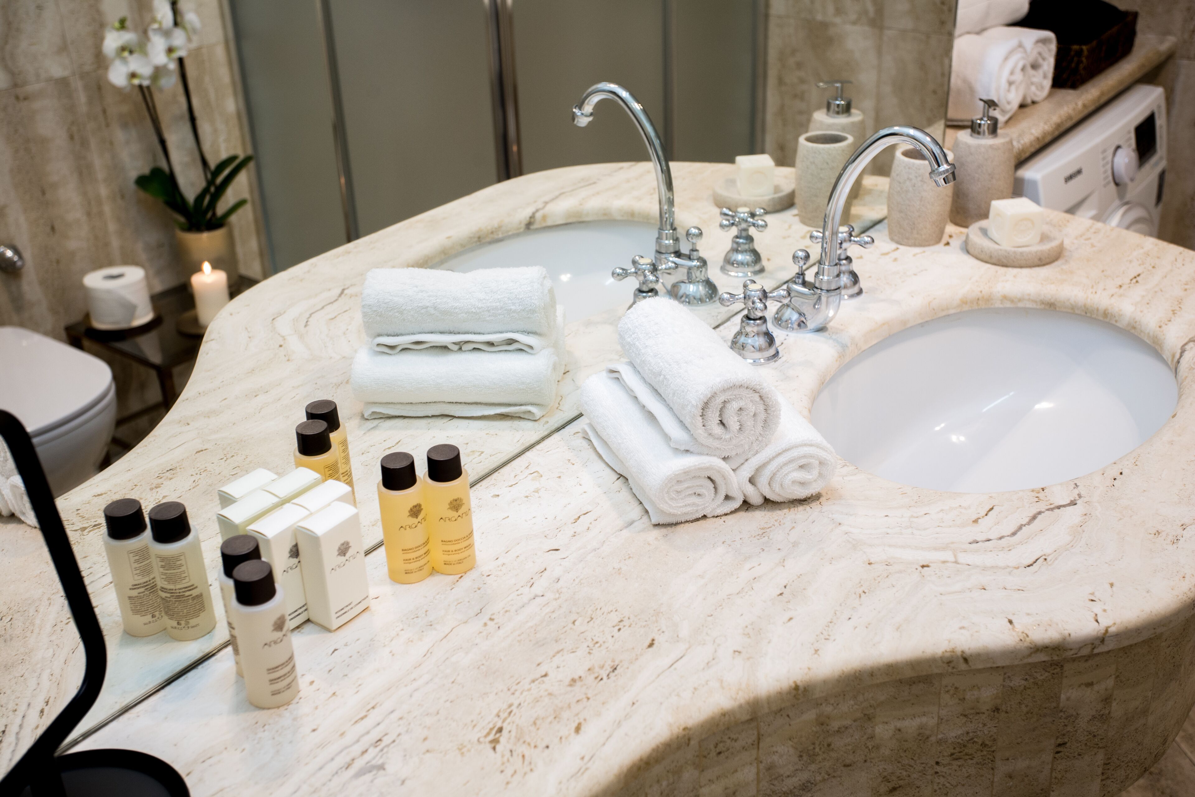 A bathroom with a marble sink, multiple towels, toiletries, and a mirror.