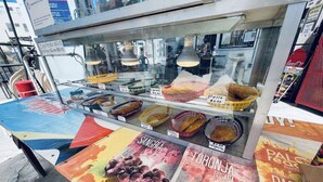 A food stall with various dishes displayed in baskets and trays, and a colorful advertisement for Sangria and Toronja Rosada.