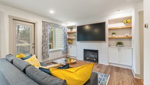 Un salon moderne avec un canapé gris, des coussins jaunes, un téléviseur à écran plat et une cheminée.