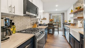Une cuisine moderne avec des armoires blanches, une cuisinière en acier inoxydable et une grande fenêtre.