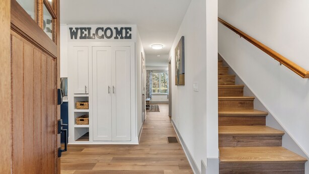 Un couloir avec une pancarte « BIENVENUE », un plancher en bois, un escalier et une vue sur un coin repas.