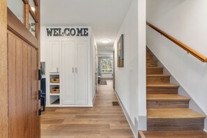 A hallway with a 'WELCOME' sign, wooden flooring, a staircase, and a view of a dining area.