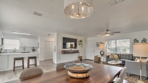 A spacious living area with a wooden dining table, a modern chandelier, and a grey sofa.