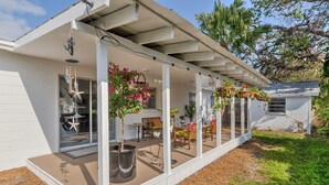 A covered patio with hanging planters, a glass door entrance, and outdoor furniture.