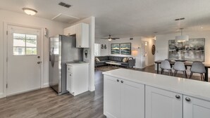 A modern kitchen with white cabinetry, a stainless steel refrigerator, and a dining area with a gray table and chairs.