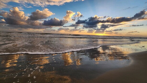 A beach with waves and a sunset.