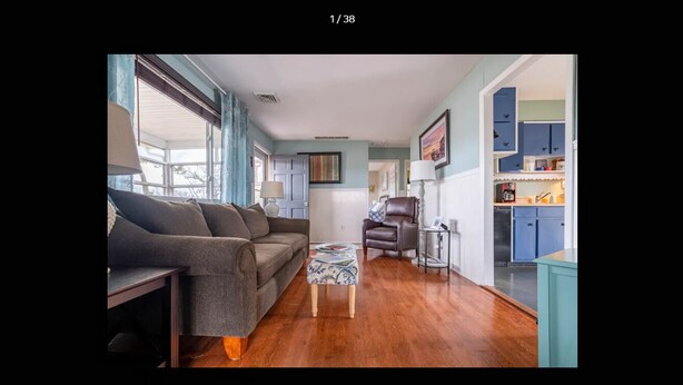 A living room with a sofa, armchair, and coffee table. There is a kitchen area with blue cabinets and a refrigerator. - The Seapointe House. DISCOVER CAPE MAY. (North cape may)