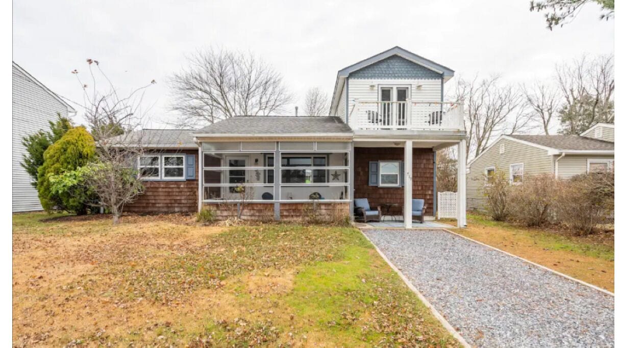 A two-story house with a front porch, a garage, and a gravel driveway.
