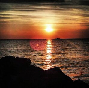 Um pôr do sol sobre o oceano com o silhueta de rochas em primeiro plano.