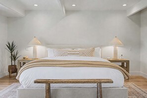 Une chambre à coucher avec un grand lit, deux tables de chevet, une commode, une lampe, une plante et un banc.