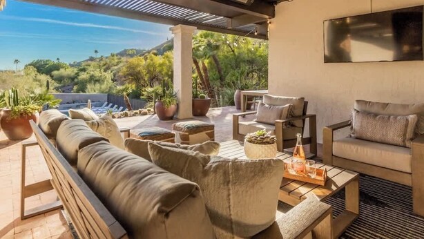 Ein überdachter Sitzbereich im Freien mit einer Couch, Stühlen und einem Tisch, mit Blick auf eine gebirgige Landschaft.
