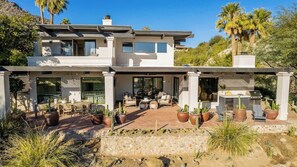 Une maison moderne à deux étages dotée d’un patio aménagé avec des meubles d’extérieur et des plantes en pot.