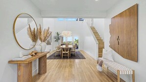 Ein geräumiger Raum mit Holzboden, einem Essbereich mit Tisch und Stühlen, einem großen Spiegel und einer Treppe zu einer weiteren Ebene.