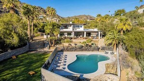 Ein modernes Haus mit Swimmingpool, umgeben von einer Steinmauer und Palmen.
