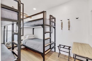 Ein Stockbett mit Schreibtisch und Ventilator, weiße Wände und ein kleiner Tisch.