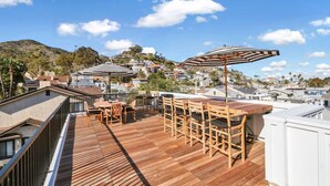 A rooftop terrace with wooden flooring, outdoor furniture, and striped umbrellas.