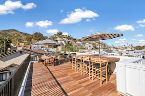 A rooftop terrace with wooden flooring, outdoor furniture, and striped umbrellas.