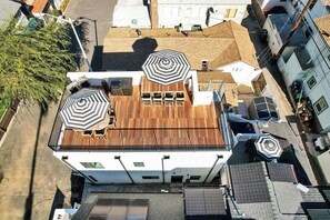 A multi-story building with a rooftop terrace featuring two large black and white striped umbrellas, a wooden deck, and a view of adjacent buildings.