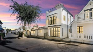 A two-story white building with a balcony and a large window on the ground floor. - Remodeled Rooftop Deck Home | Casino & Ocean Views (Avalon)
