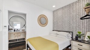 A bedroom with a bed, a bedside table with a plant, a mirror, and a wardrobe. - Remodeled Rooftop Deck Home | Casino & Ocean Views (Avalon)