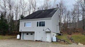 A two-story house with a sloped roof, a front porch, and a garage. - Condo near wiffletree chairlift! (Carrabassett Valley)