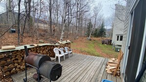 A wooden deck with a grill, chairs, and a stone wall. - Condo near wiffletree chairlift! (Carrabassett Valley)
