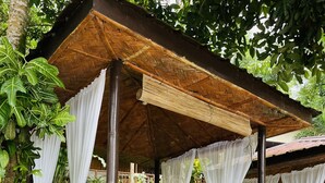 Un pabellón de madera con techo de paja, cortinas blancas y una mesa para picnic.