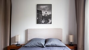 Ett sovrum med en säng, två sängbord, en lampa på varje bord och en inramad bild av Eiffeltornet på väggen.