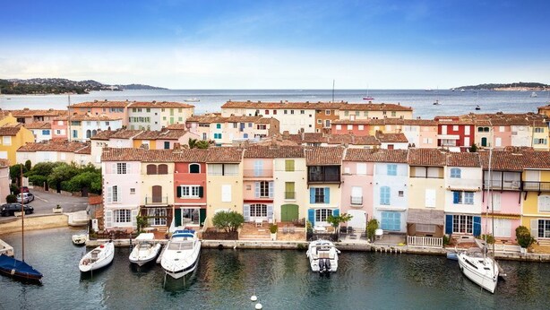 Une ville côtière aux bâtiments aux couleurs vives, un port de plaisance rempli de bateaux et une vue dégagée sur la mer.