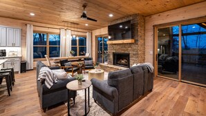 A spacious living room with a fireplace, a large TV mounted on a stone wall, and a cozy seating area with a sofa and chairs.