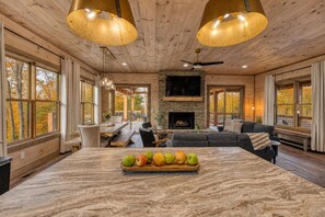 A spacious living area with a fireplace, large windows, and a marble island with fruit.
