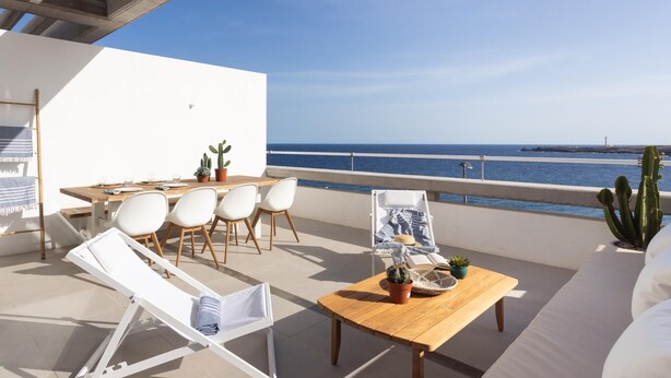A terrace with a wooden table, white chairs, a lounge chair, and a view of the sea. - Superior Seafront Apartment, Porís 6 (Porís de Abona)