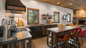 A modern kitchen with a central island, wooden cabinets, and a stone fireplace. - Lake Side, Paddleboards, Firepit, Basketball! (Durango)