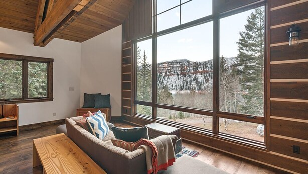 A cozy living room with a large window, wooden beams, and a sofa with pillows. - Lake Side, Paddleboards, Firepit, Basketball! (Durango)