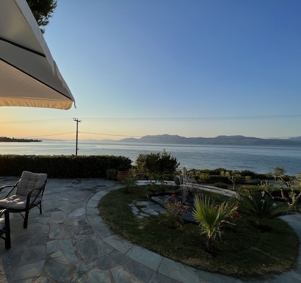 A patio with a chair, a small garden, and a view of the sea and mountains.