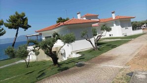 Una casa de dos pisos con tejado de tejas rojas, paredes blancas y entrada pavimentada.