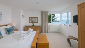 Une chambre d’hôtel équipée d’un lit, d’une table de chevet, d’une lampe, d’un miroir et offrant une vue sur la mer grâce à de grandes fenêtres.