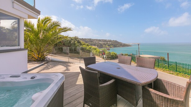 Une terrasse extérieure avec un jacuzzi, des meubles en osier et une vue sur la mer.