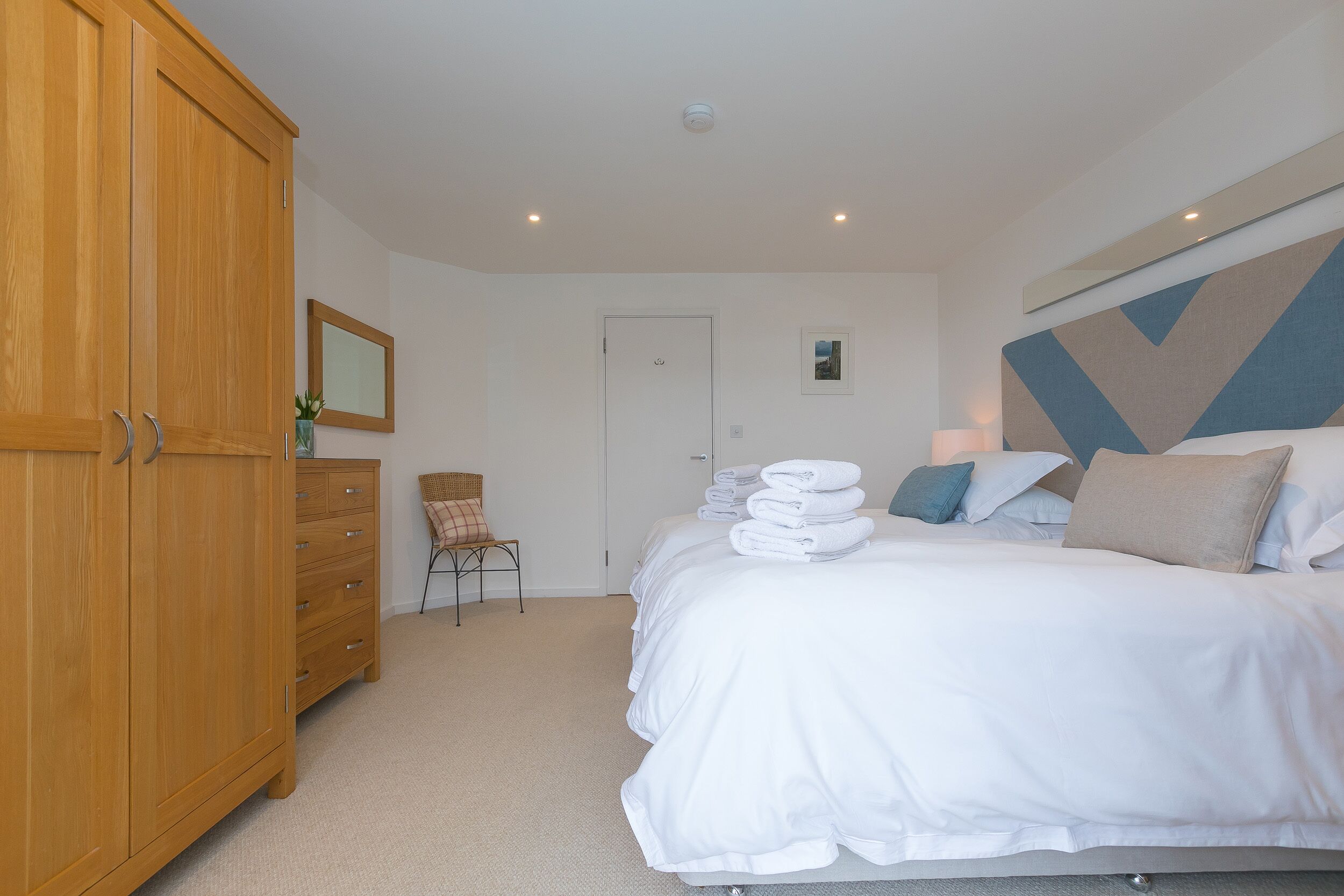 A bedroom with a bed, a wooden wardrobe, a chair, and a door.