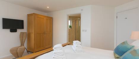 A bedroom with a bed, a wooden wardrobe, a television, and a bathroom visible through an open door.