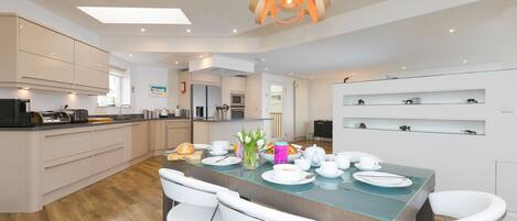 A modern kitchen with a central island, white cabinetry, and a dining area with a glass table and white chairs.