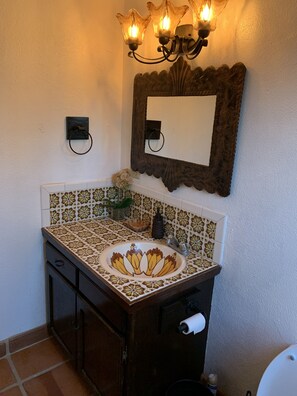 Een badkamer met een decoratieve wastafel, een spiegel met een decoratieve lijst en een wandlamp.
