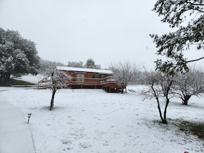 A wooden cabin with a deck, surrounded by snow-covered ground and trees.