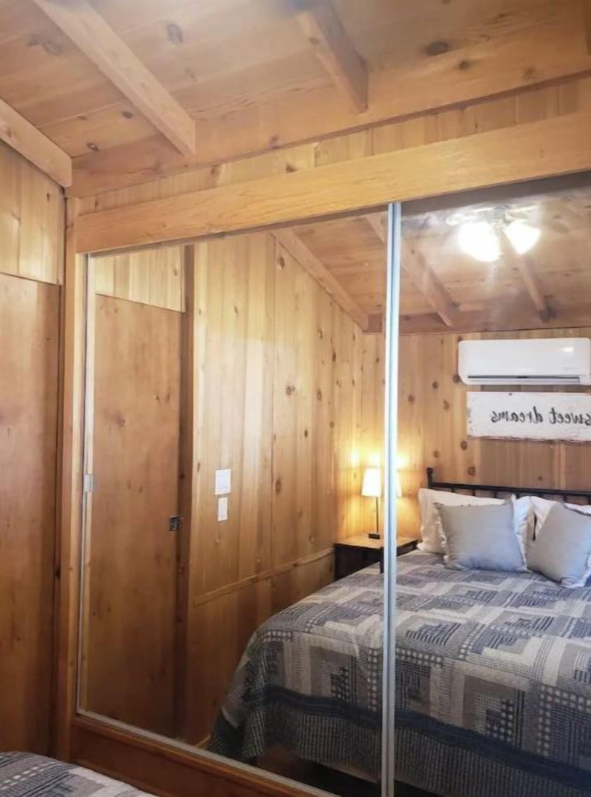 A wooden-paneled room with a bed, a nightstand, and a wall-mounted air conditioning unit.