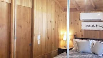 A wooden-paneled room with a bed, a nightstand, and a wall-mounted air conditioning unit.